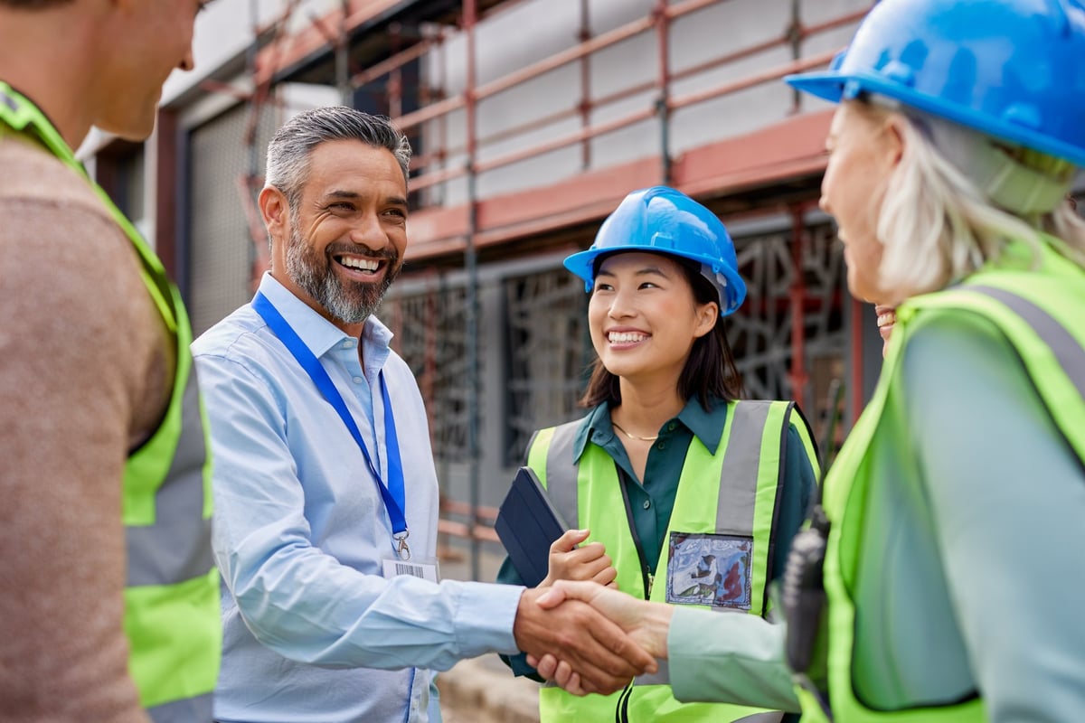 A construction manager and architect shaking hands on a building site after agreeing the paperwork